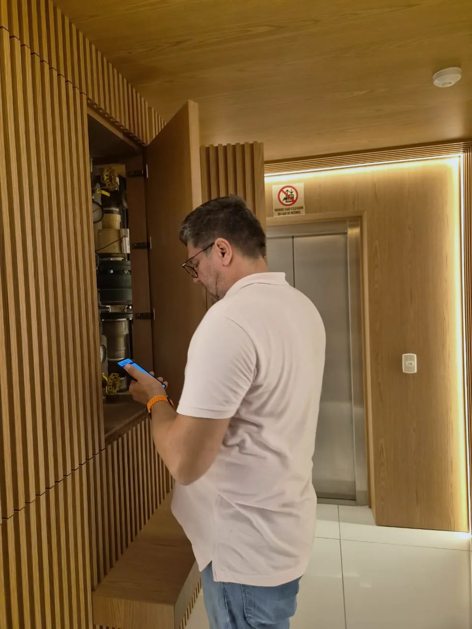 Eduardo Marinho, fundador da Acquameter, conferindo o app ao lado do quadro de hidrômetros no hall de um condomínio